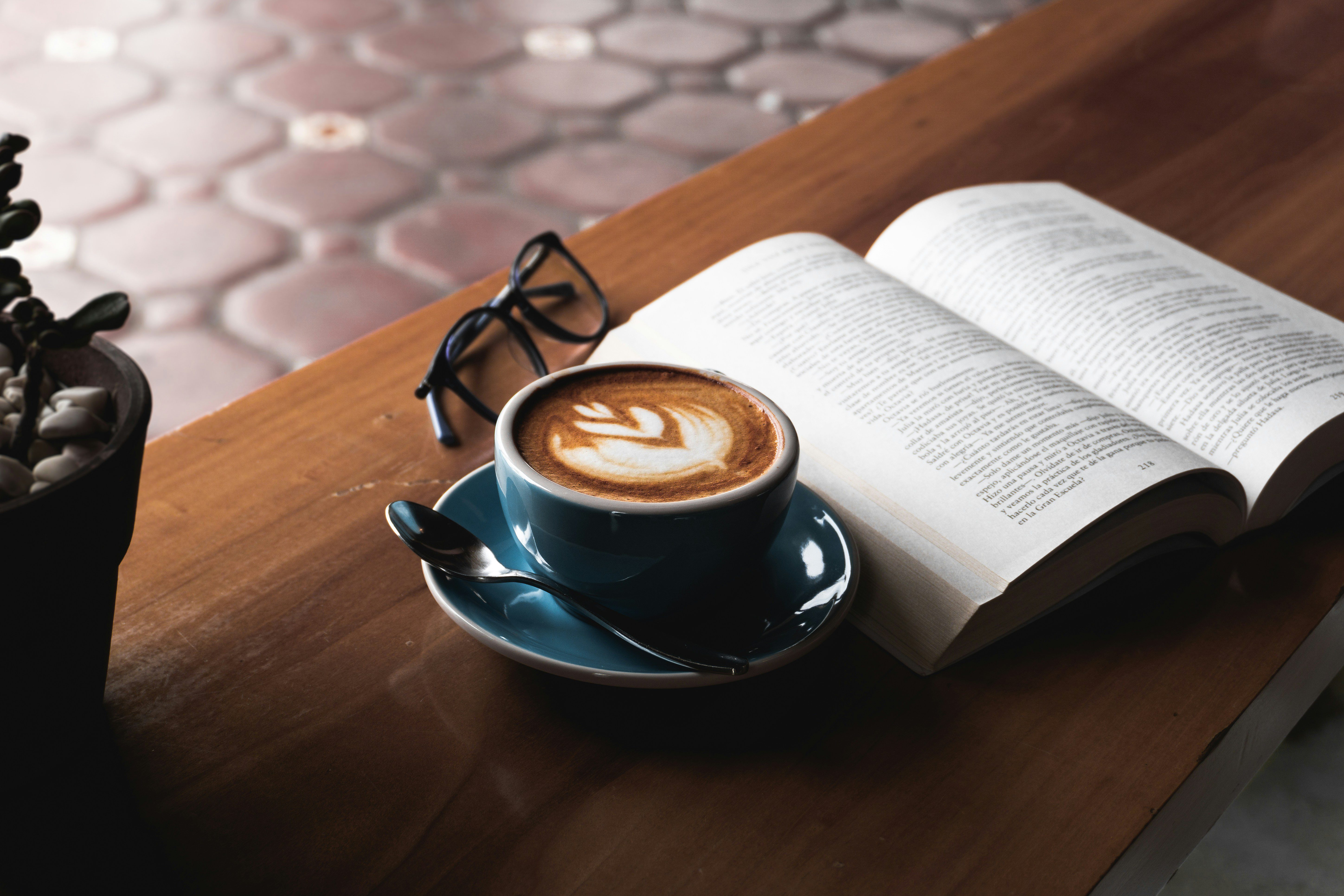 Cappuccino ja avoinna oleva kirja pöydällä, sekä lukulasit